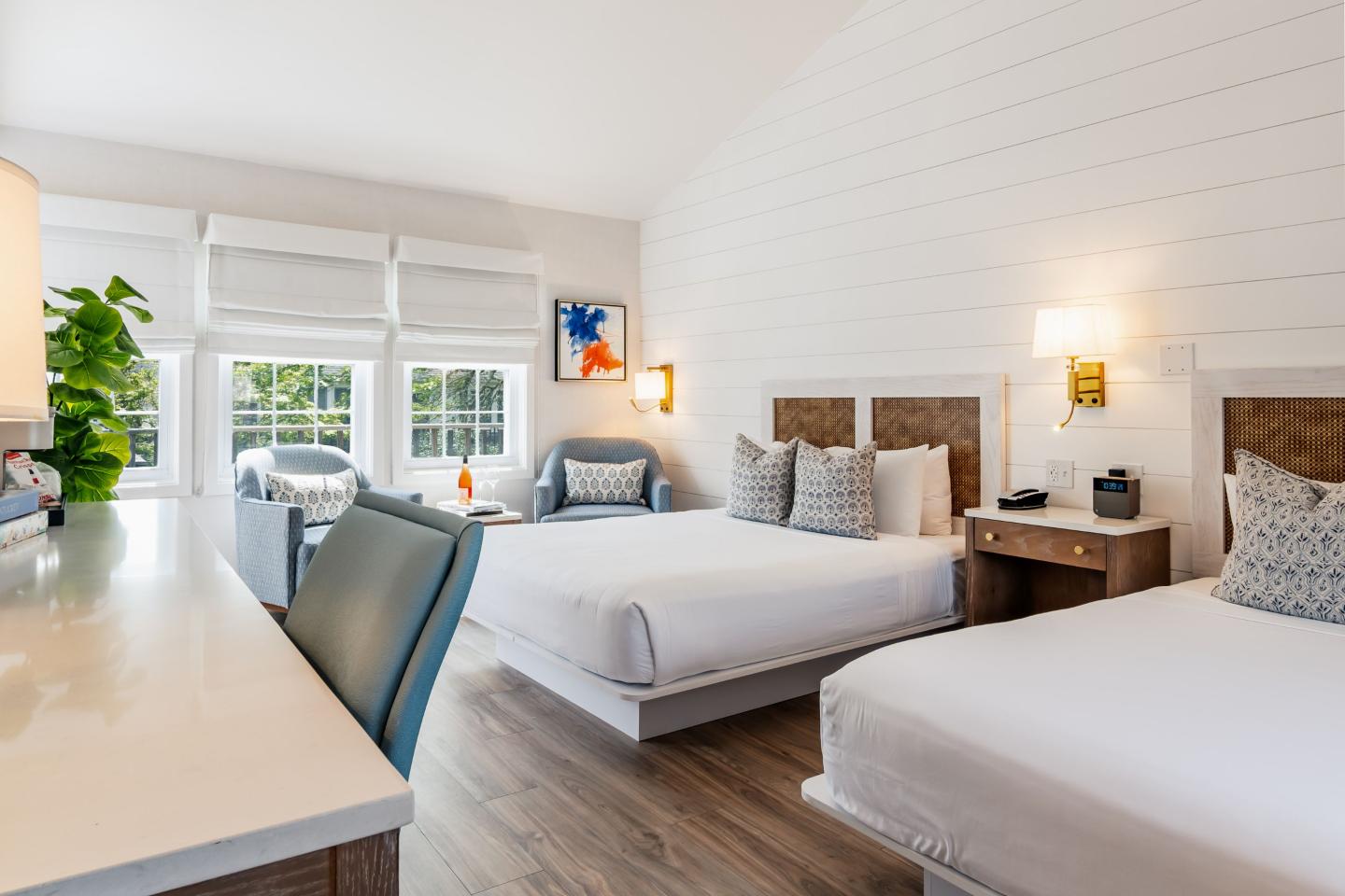 Bright hotel room with two beds, a desk, and a sitting area with large windows.