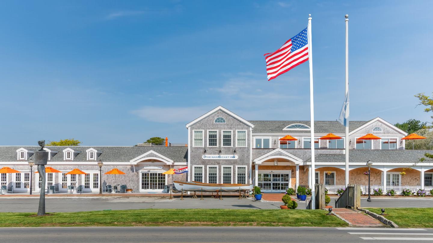 Hotel with gray shingles, orange parasols, and American flag under clear blue sky.