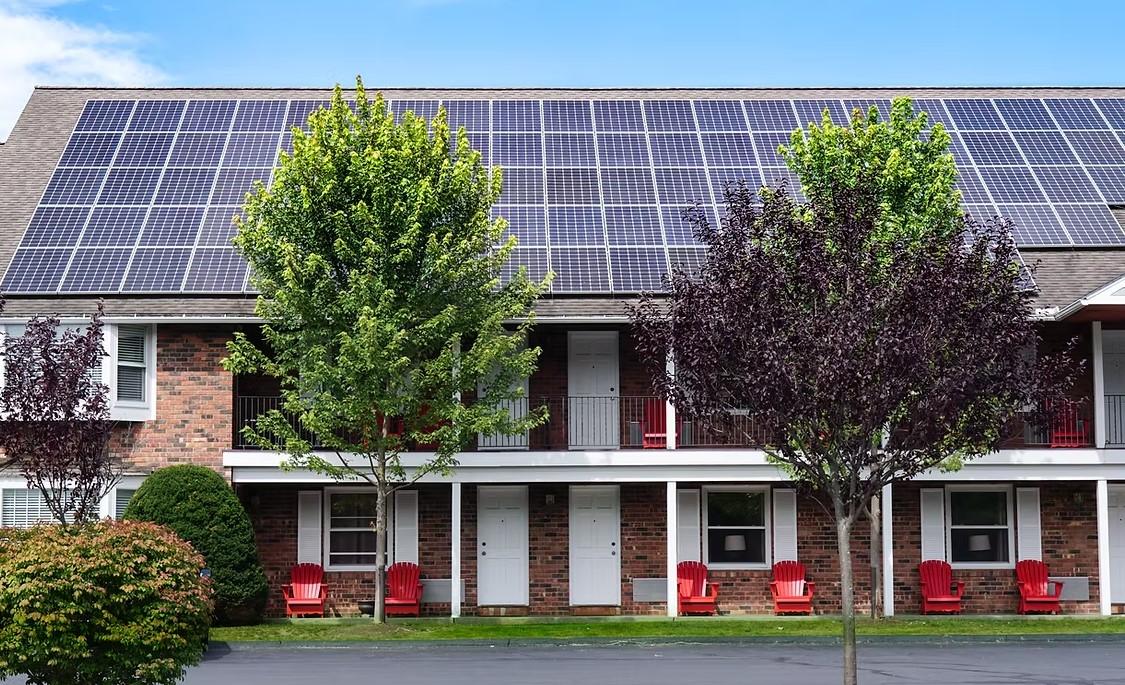 Brick building with solar panels, trees, and red chairs on a lawn.