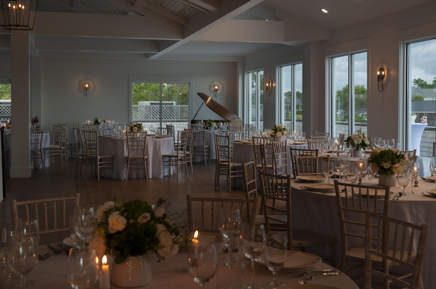 Dimly lit dining room with elegantly set tables and large windows.