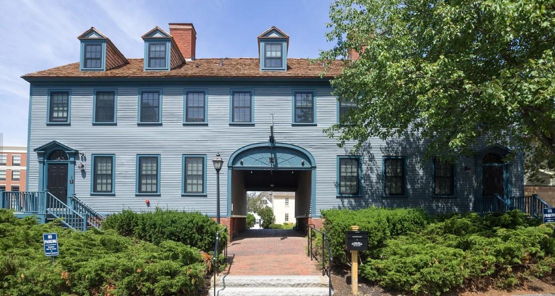 Blue colonial house with brick path and green bushes under clear sky.
