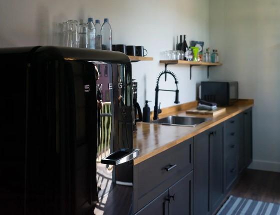 Cozy kitchen with black fridge, wooden countertop, and shelves with bottles and mugs.