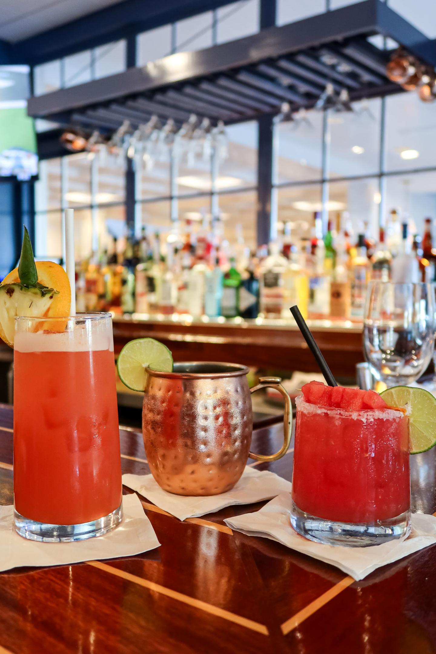 Three colorful cocktails on a bar counter, garnished with fruit slices.