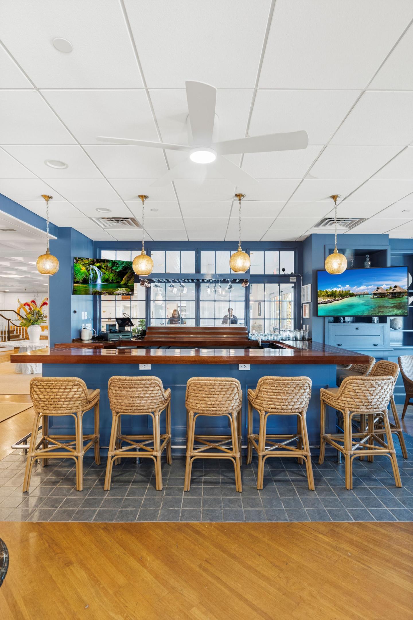 Bar area with wicker stools, blue walls, and hanging pendant lights.