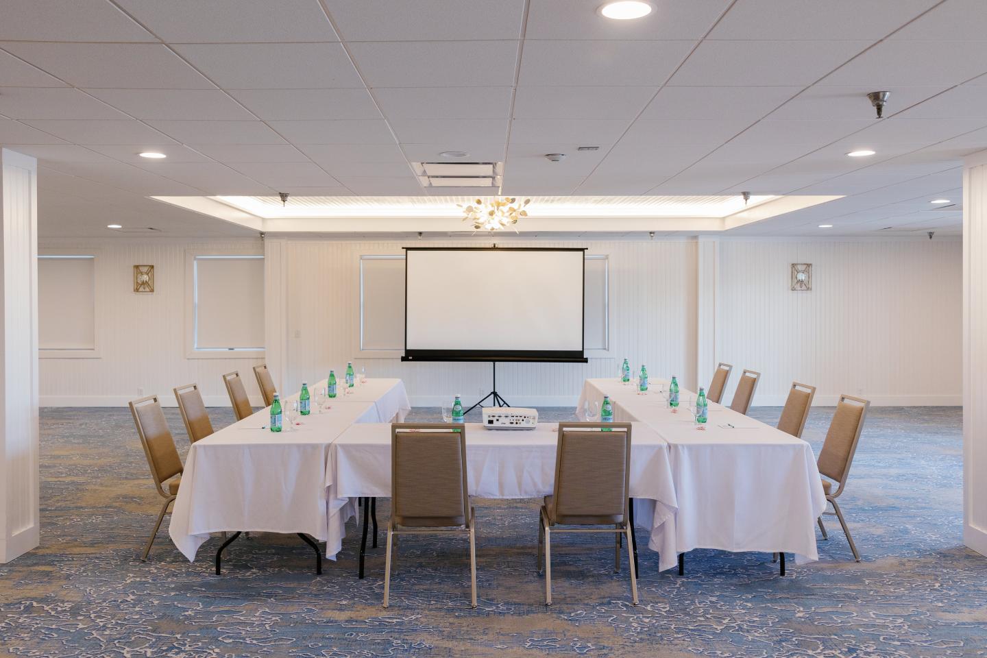 Conference room with U-shaped table, chairs, and projector screen.