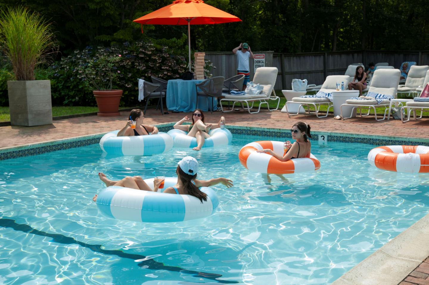 People relax on pool floats in a sunlit backyard pool.
