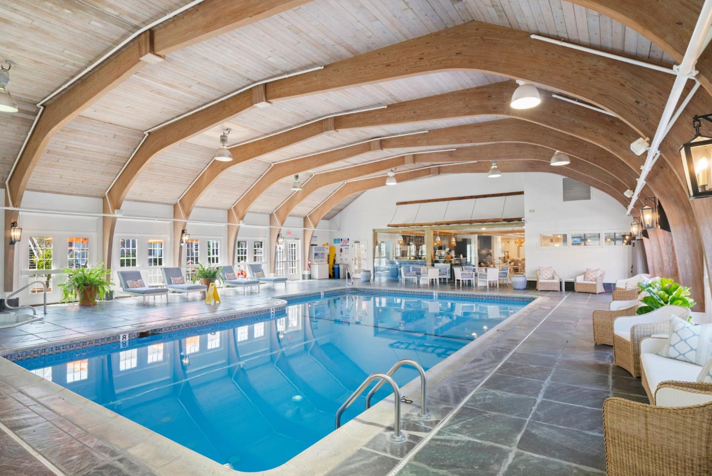 Indoor pool area with wooden beams, lounge chairs, and a small bar.