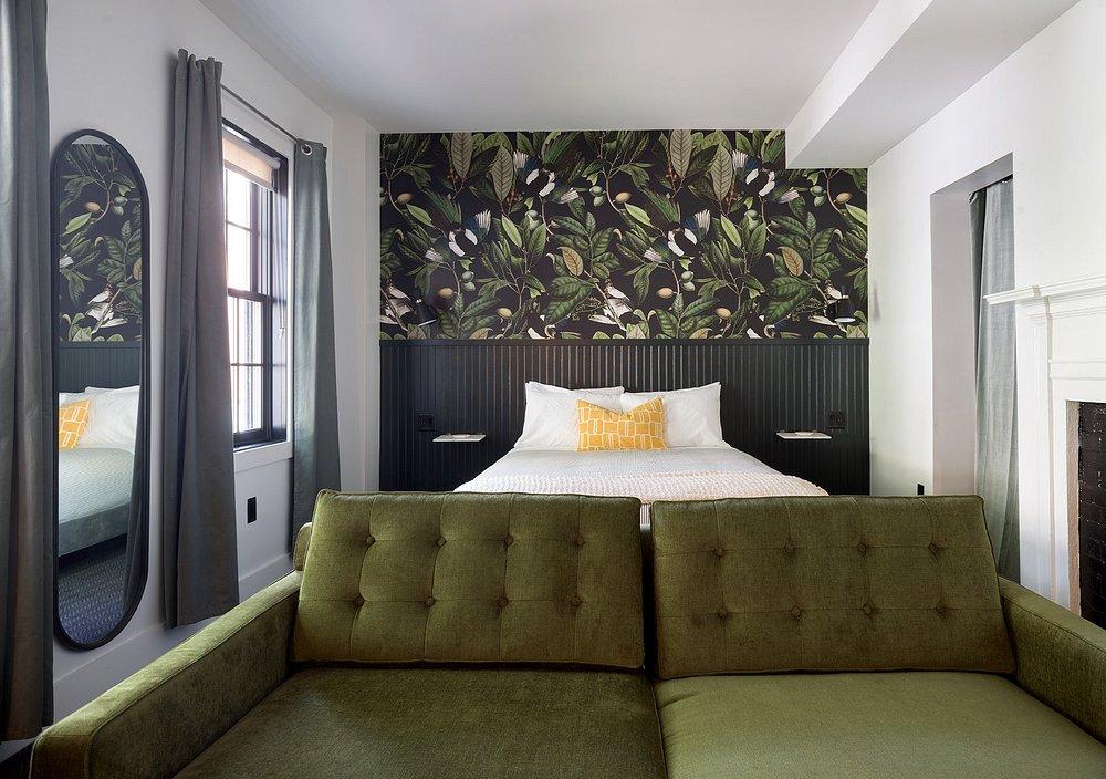 Cozy bedroom with green couch, bed, and botanical wallpaper.