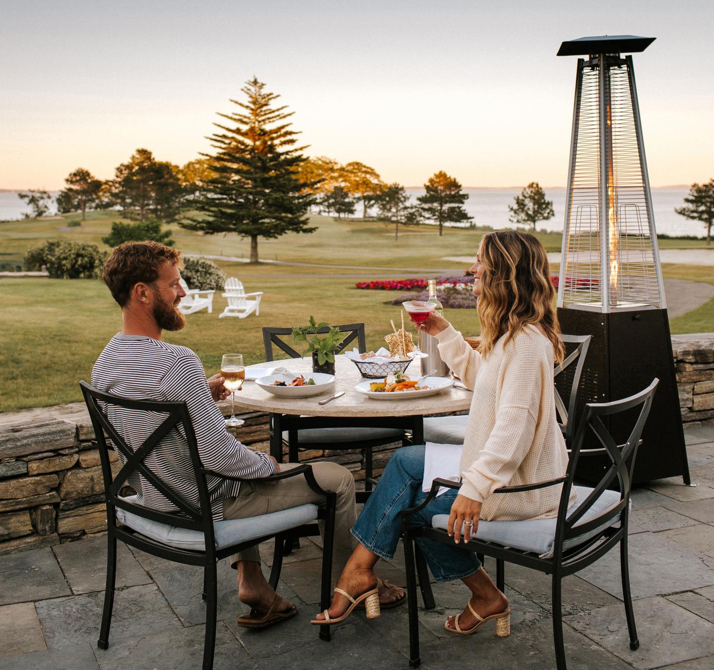 Couple dining outdoors at sunset near a garden and trees.
