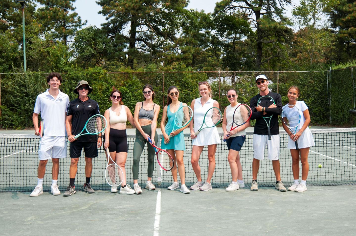 Tennis players pose on a court, holding rackets, smiling.