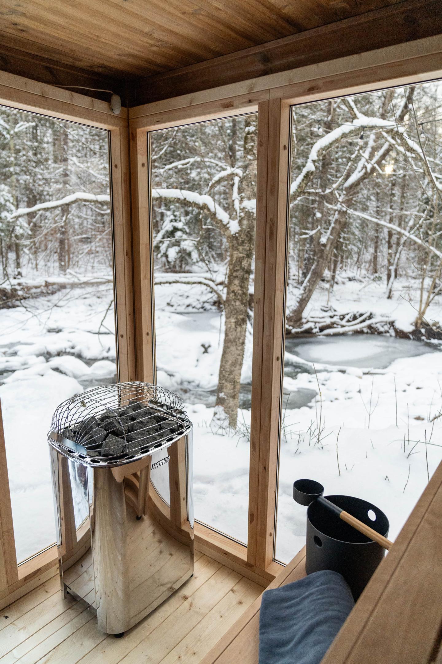 Cozy sauna room with snowy forest view through large windows.