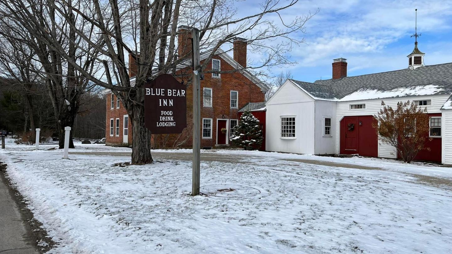 Snow-covered ground with a red brick building and a wooden sign.