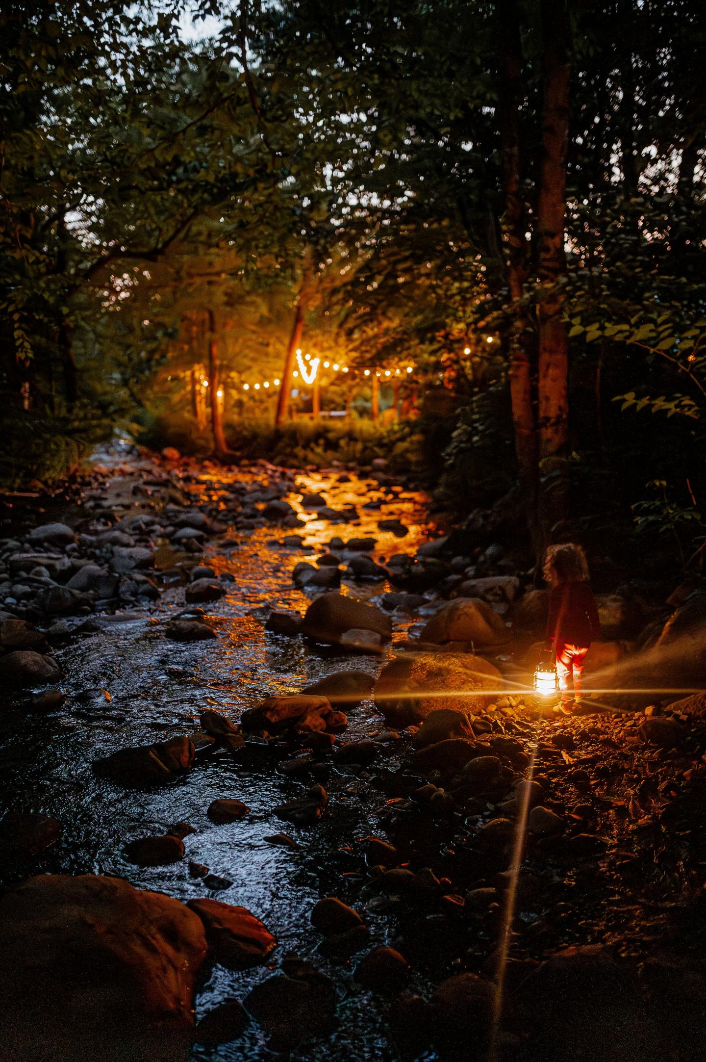 Stream at dusk with lantern and warm lights in the background.