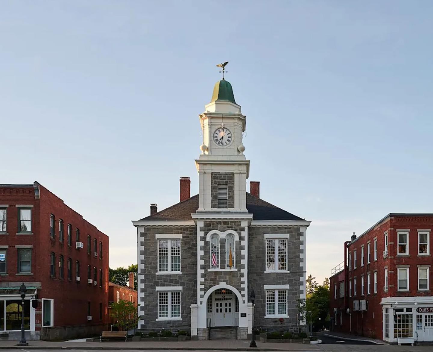 Historic brick building with a clock tower and weather vane, flanked by red buildings.