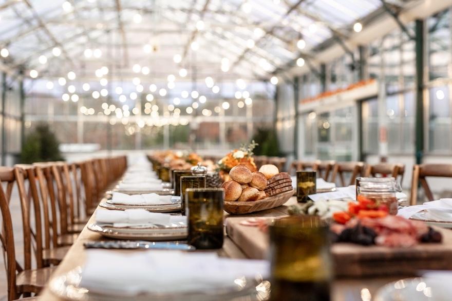 Elegant table setting in a greenhouse with lights and food platters.