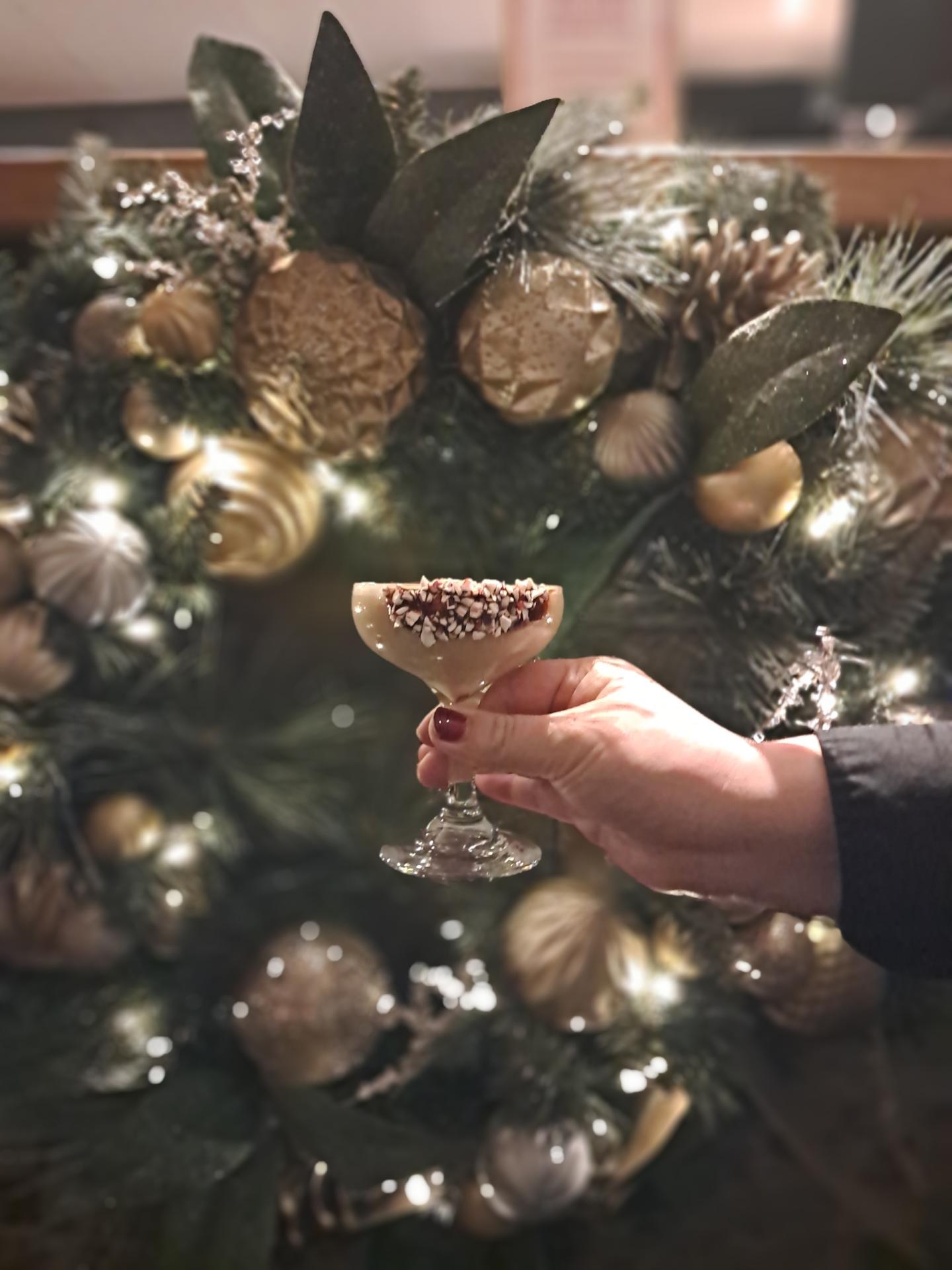 Hand holding dessert glass in front of festive Christmas wreath.