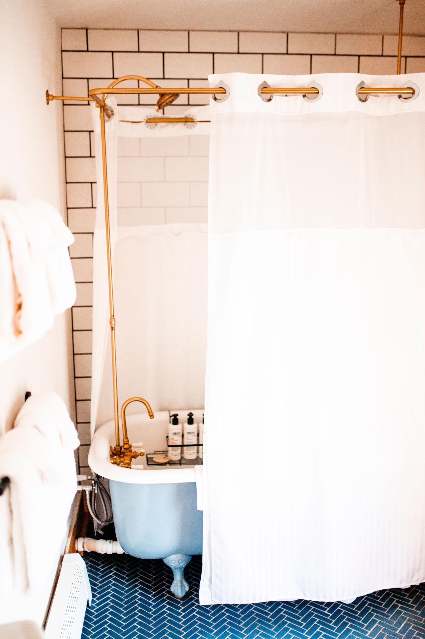 Clawfoot bathtub with white shower curtain and blue tile floor.