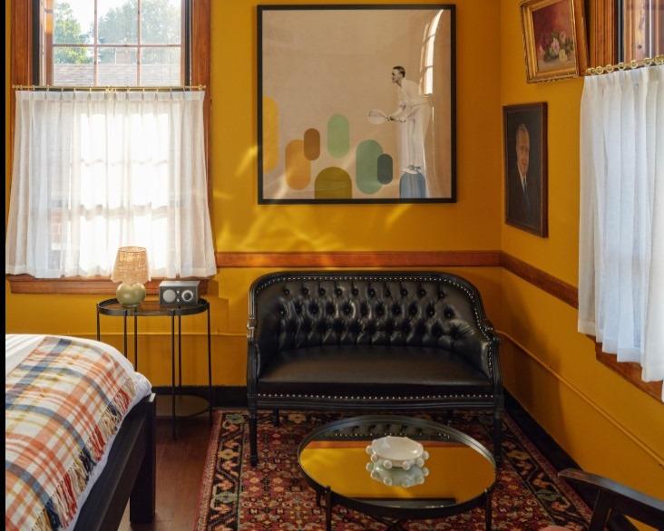 Cozy yellow room with a black sofa, colorful rug, and framed artwork.