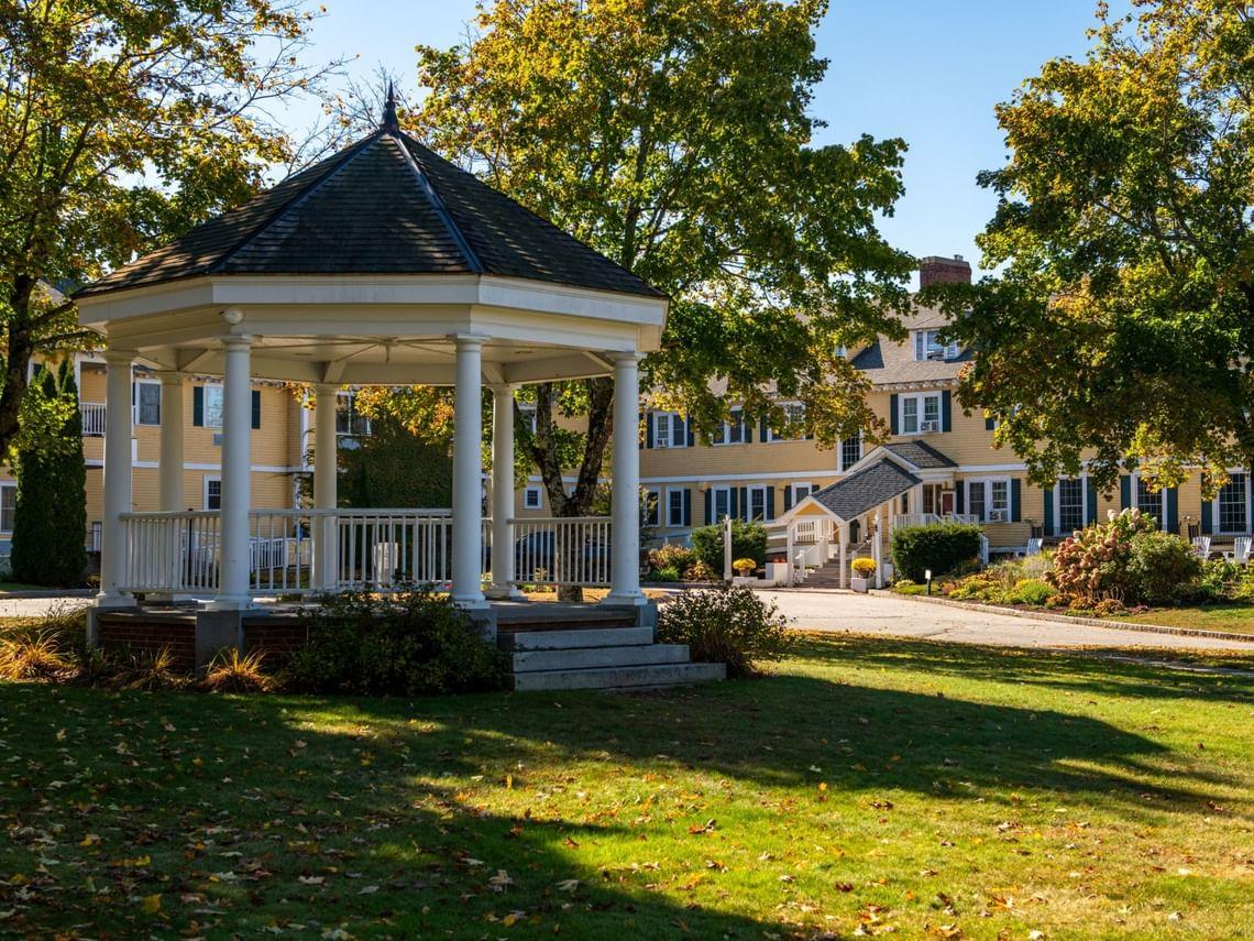 White gazebo and a yellow building with trees on a sunny day.