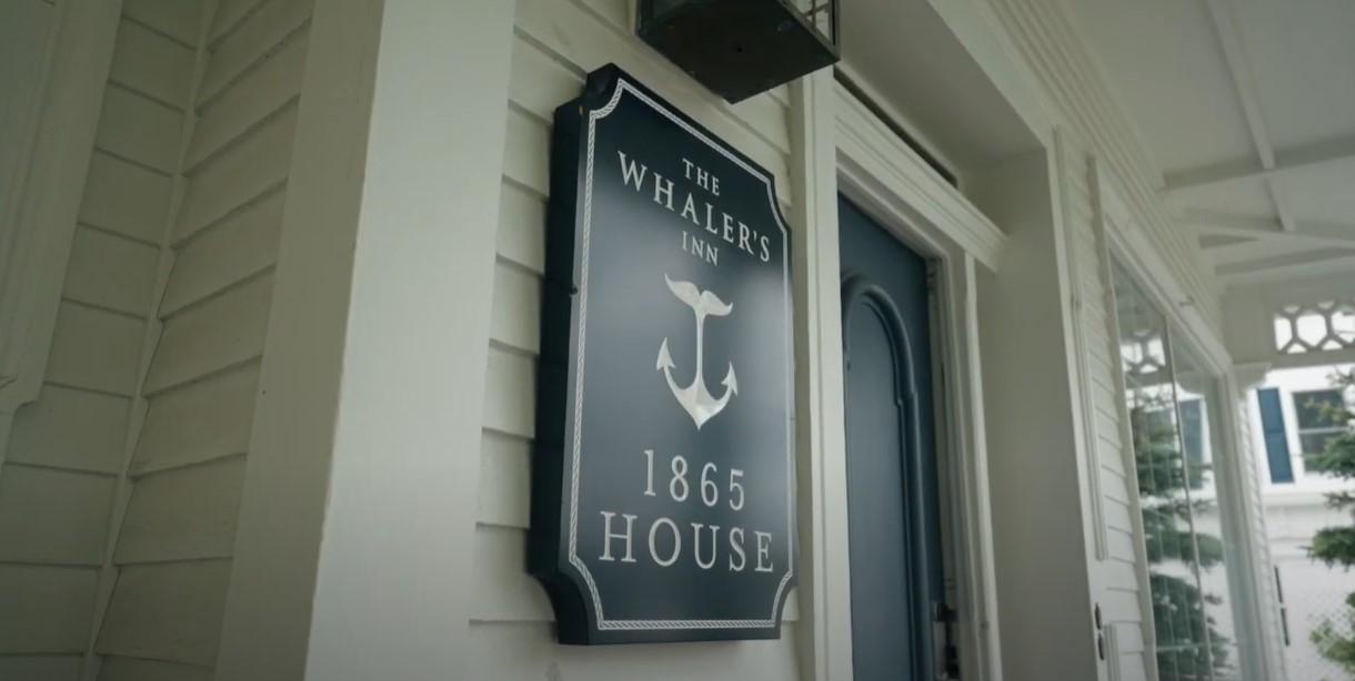 Historic house sign on white exterior wall beside door.