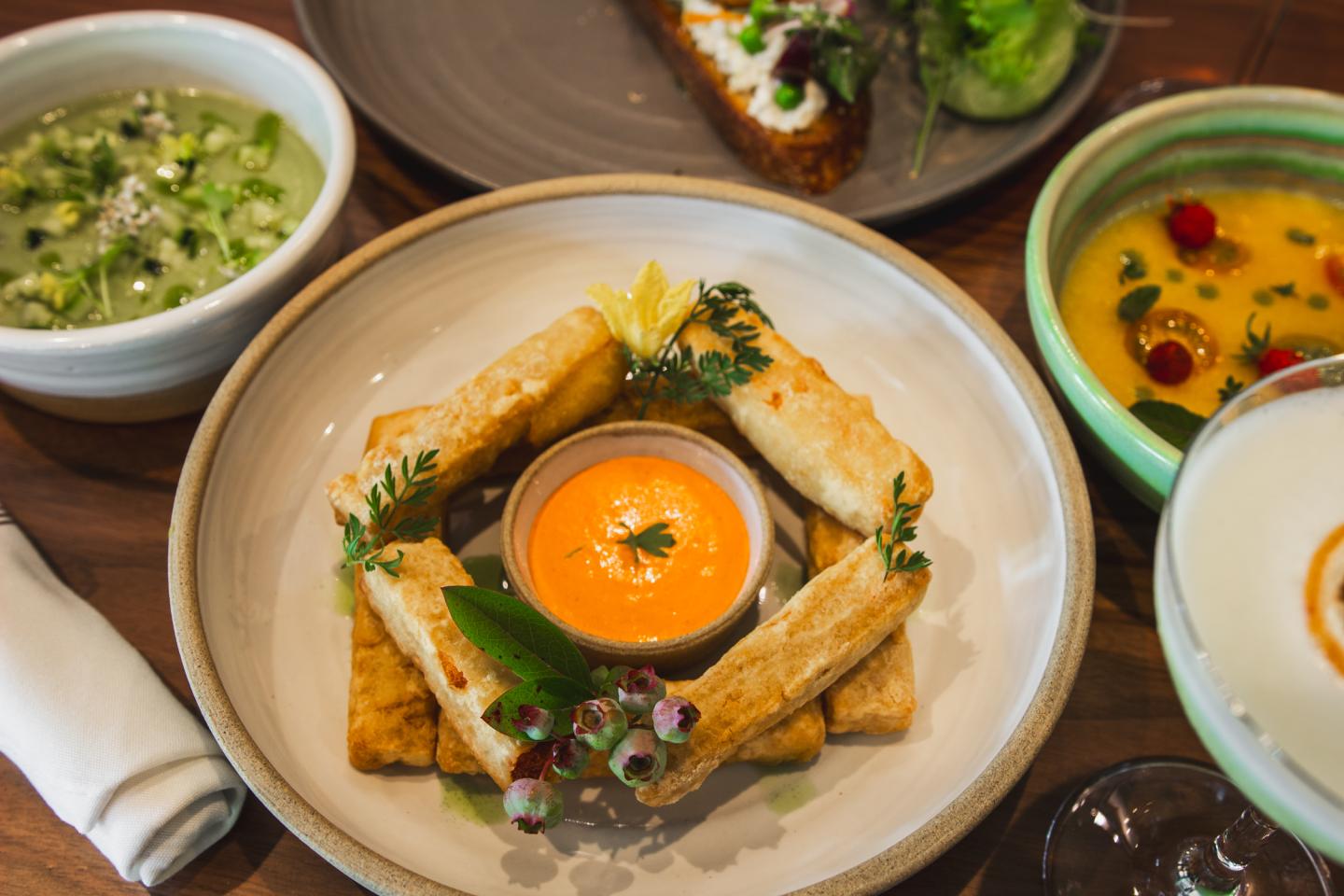 Assorted dishes including cheese sticks and colorful soups on a wooden table.