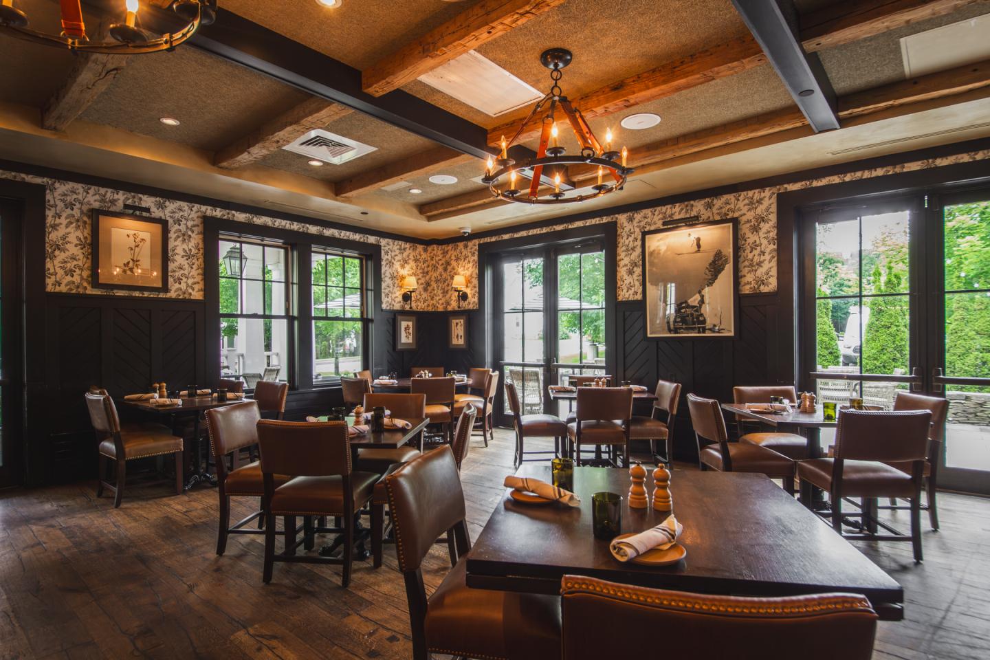 Cozy restaurant interior with wooden tables, chairs, and warm lighting.