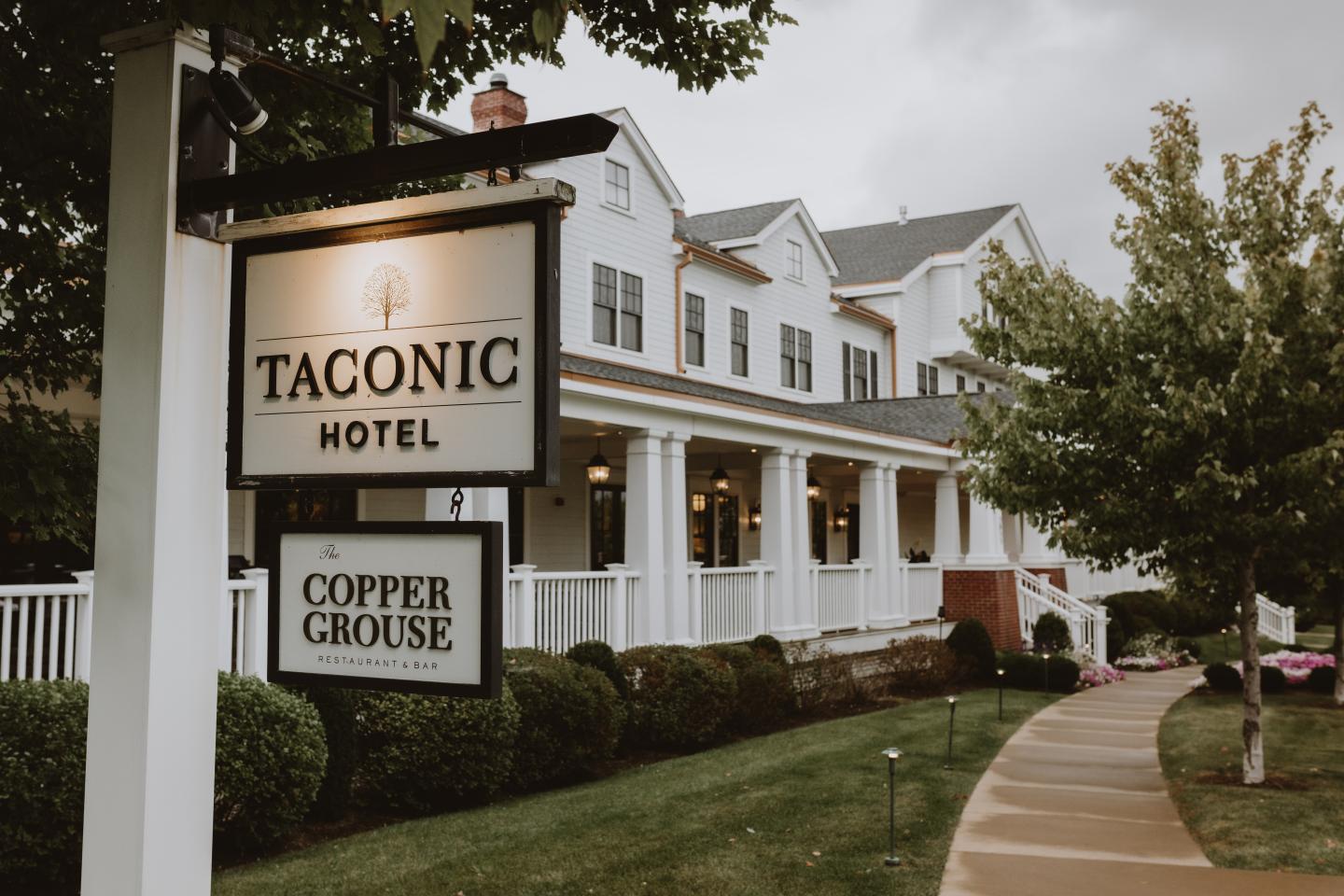 Taconic Hotel exterior with a sign and garden path.