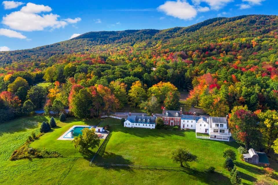 Manor with pool on lush autumn hillside under blue sky.