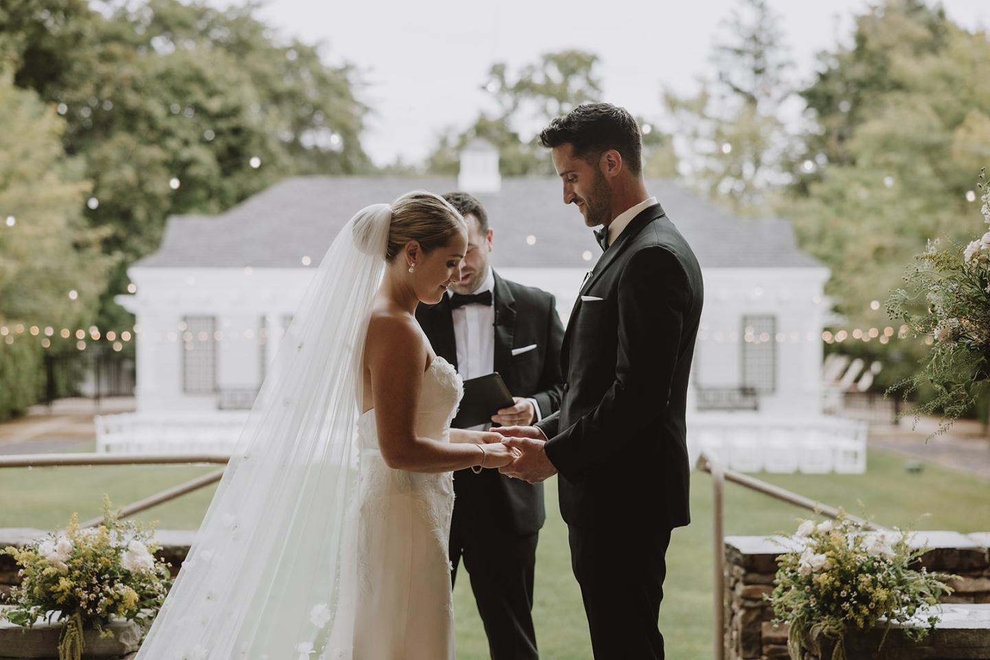 Bride and groom exchanging vows outdoors, officiant between them.