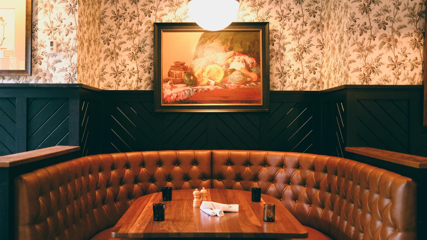 Cozy booth in a dimly lit restaurant with vintage wallpaper and framed artwork.