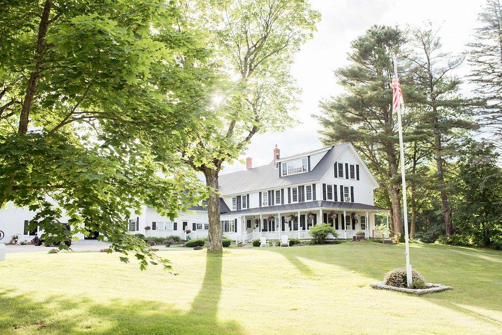 Large white house on a sunny day, surrounded by trees and a flagpole in front.