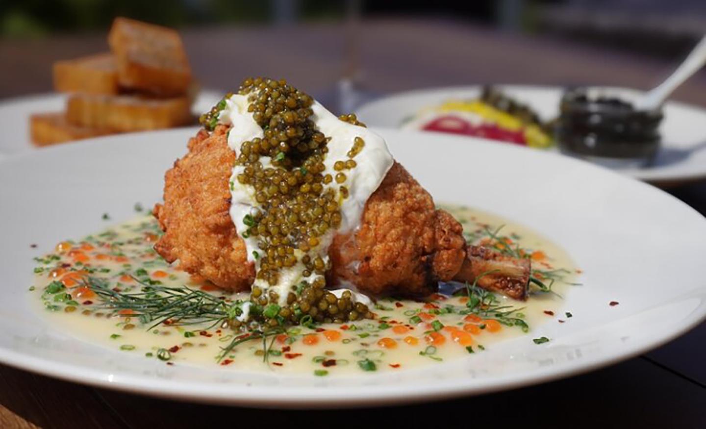 Fried chicken with sauce and garnish on a white plate, with bread slices in the background.