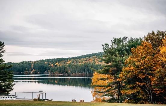 Lake with autumn trees, overcast sky, and a small dock.