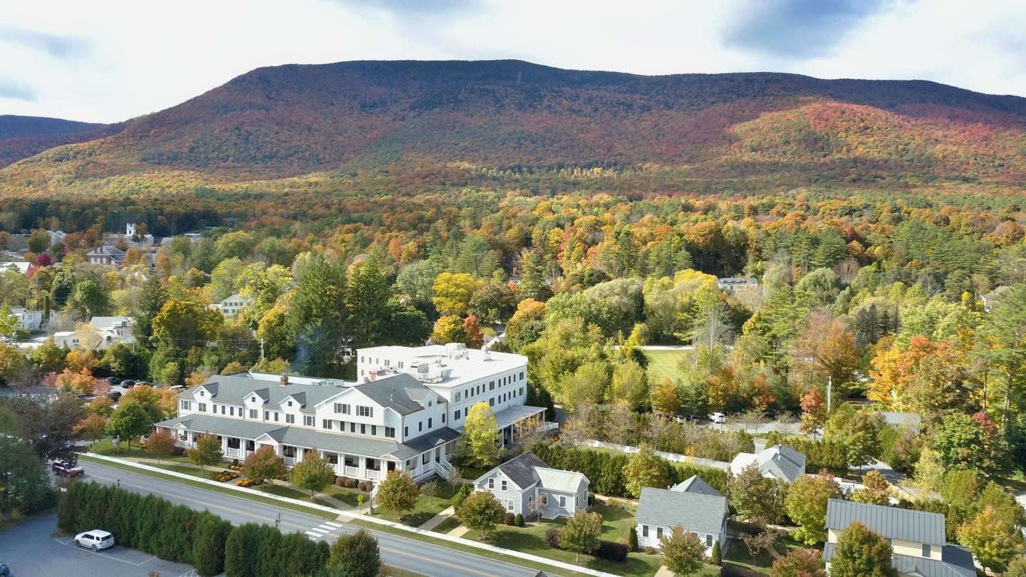 Aerial view of a town with autumn trees and mountains in the background.