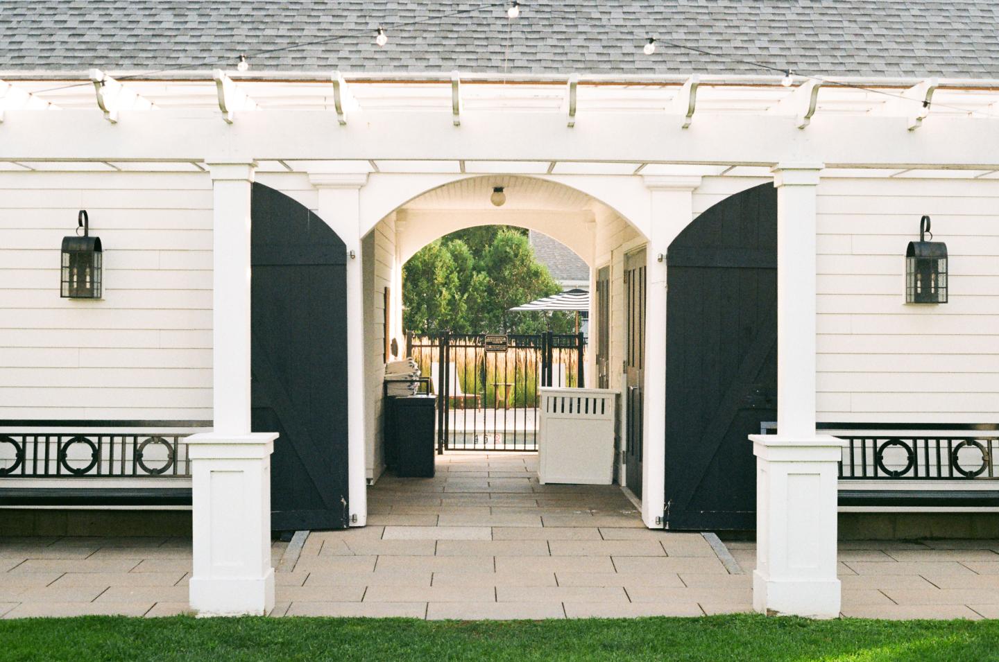 White building archway leading to a yard with trees; lanterns on each side.