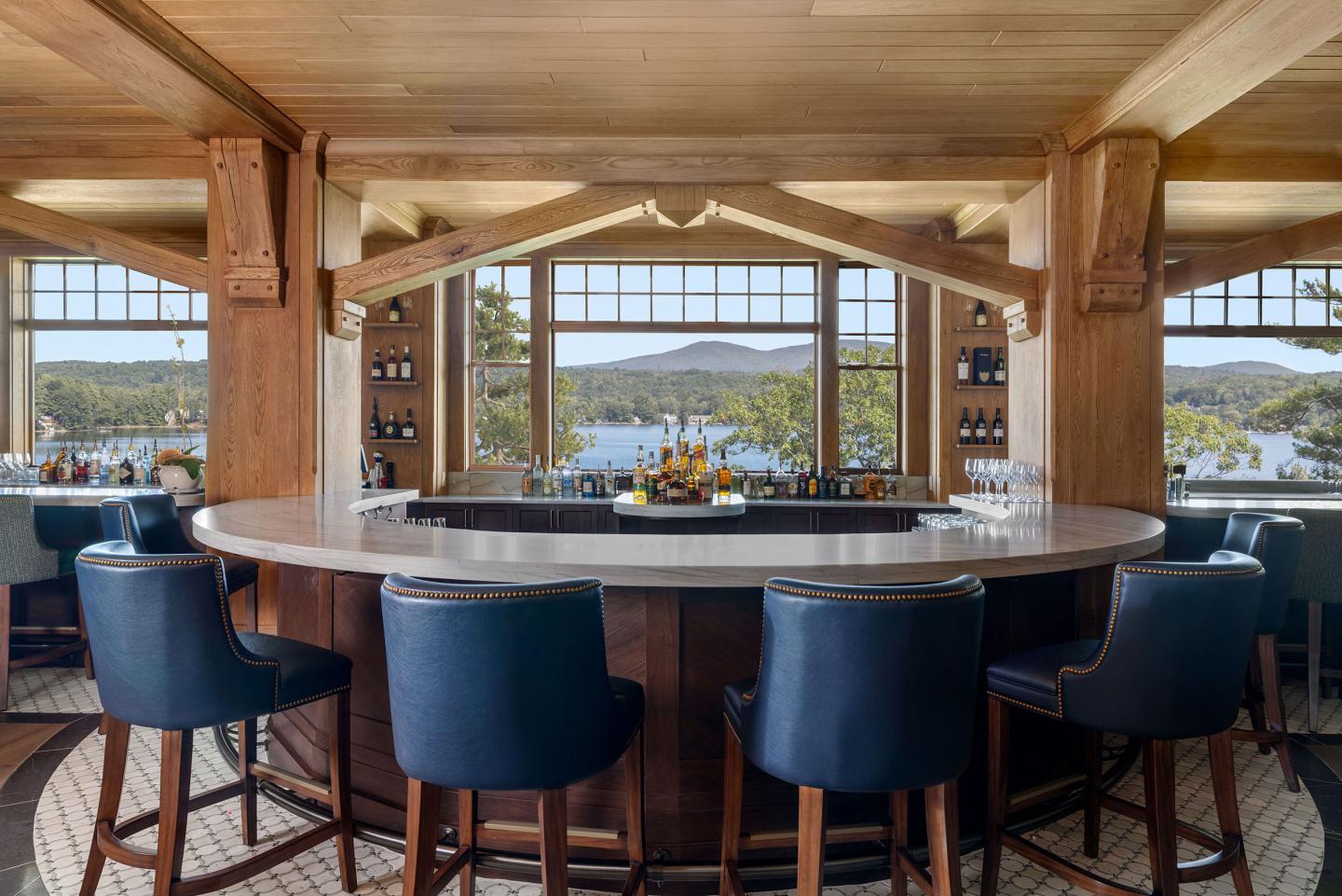 Bar with blue stools and large windows overlooking a scenic view of hills and water.