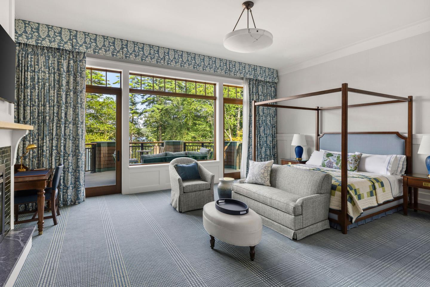 Spacious bedroom with canopy bed, sofa, large windows, and a view of trees.