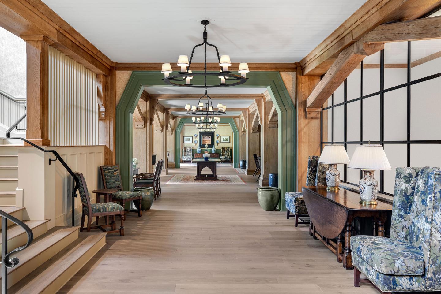 Elegant hallway with wooden beams, chandeliers, and blue-patterned chairs.