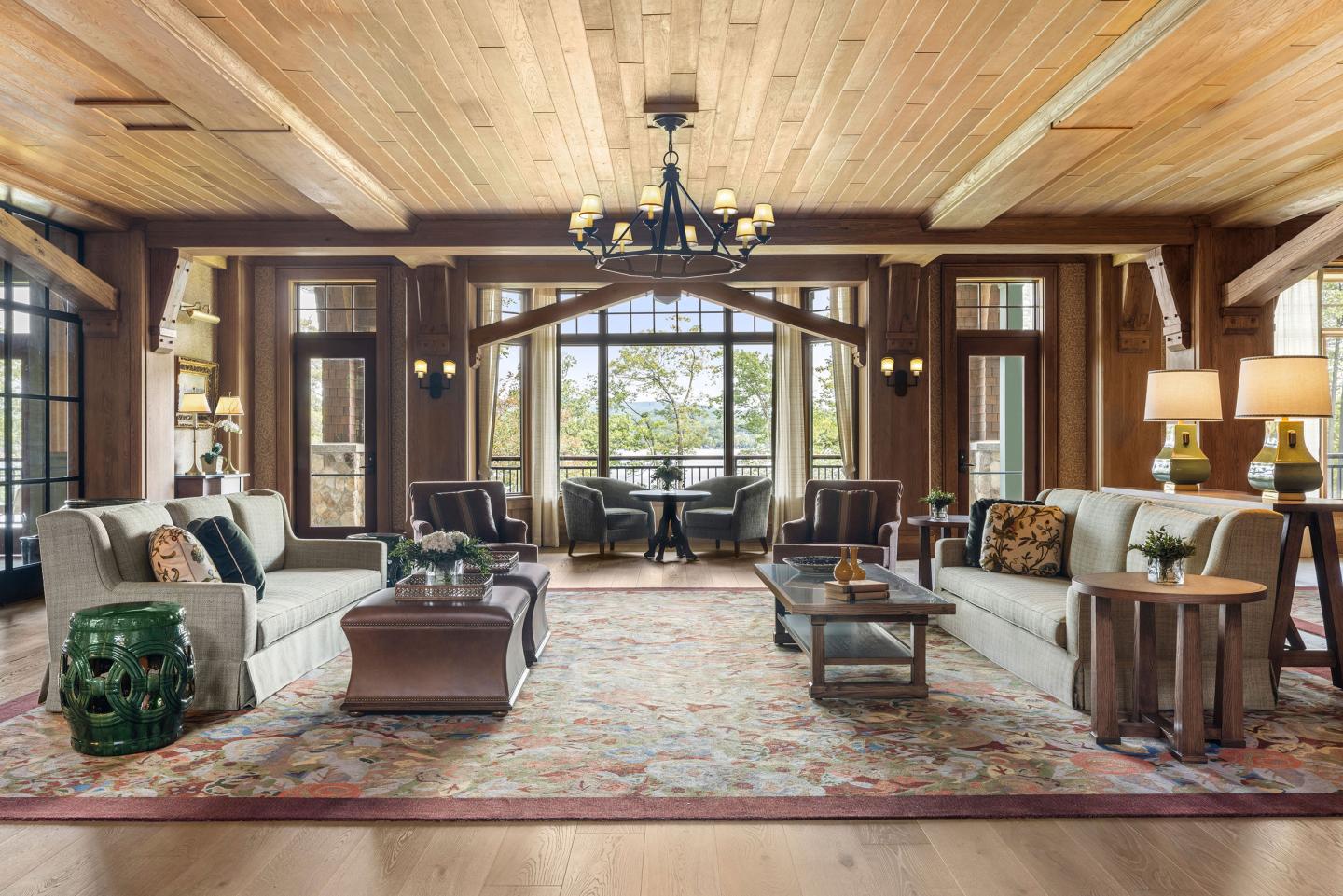 Spacious, cozy living room with sofas, wooden ceiling, large windows, and a central chandelier.