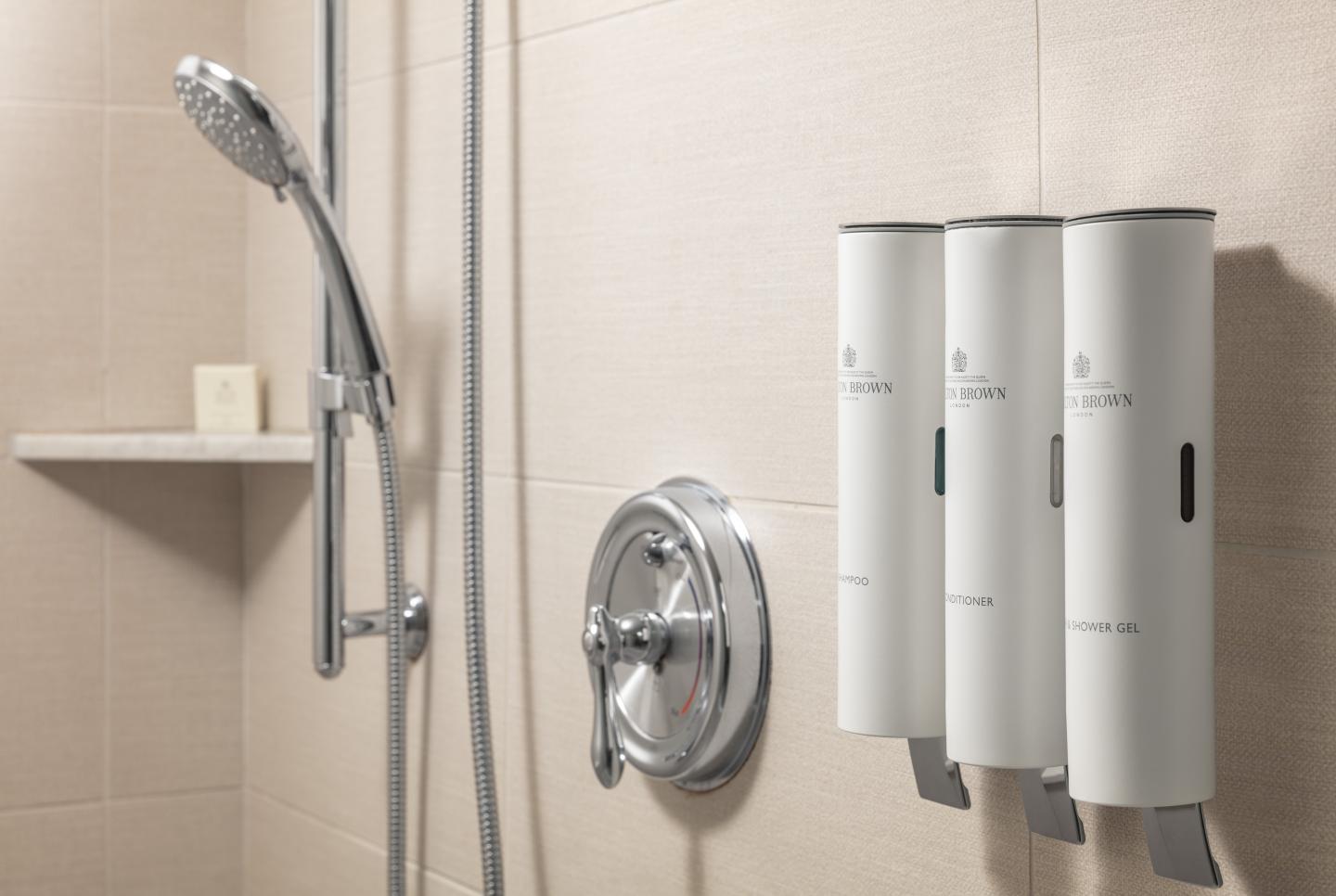 Shower with handheld head, three wall-mounted soap dispensers.