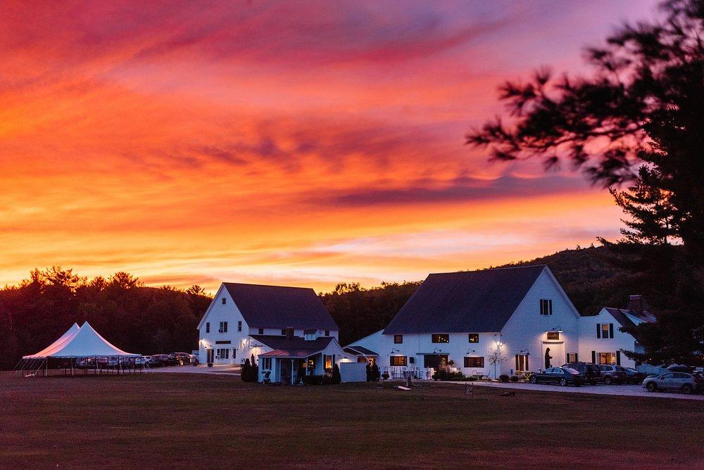 Sunset over farmhouse and tent with vibrant orange sky.