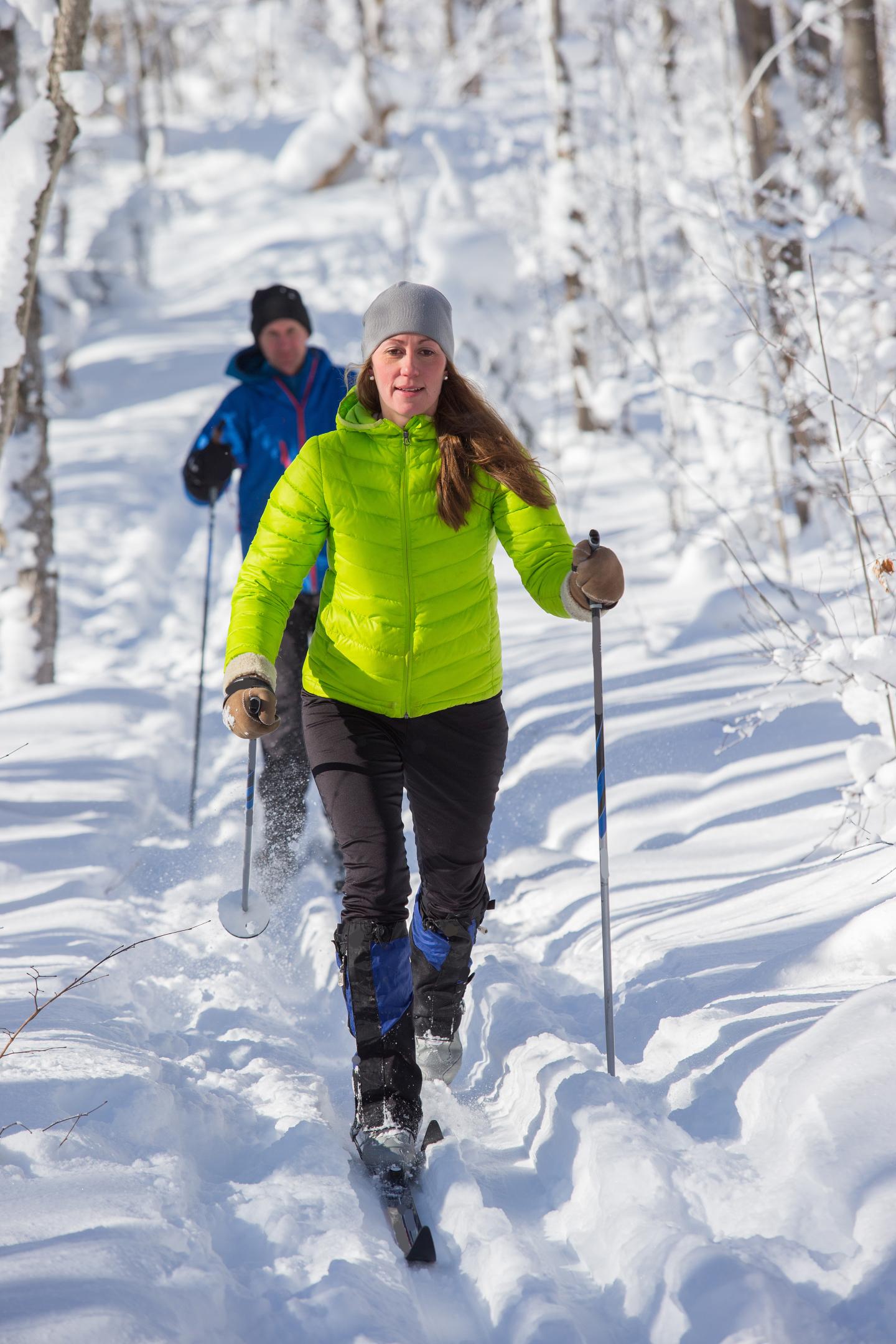Two people cross-country skiing through a snowy forest trail.