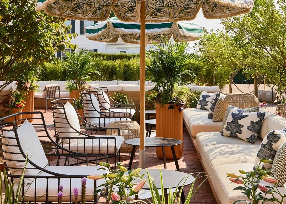 Sunny patio with cushioned seating, potted plants, and a large parasol.