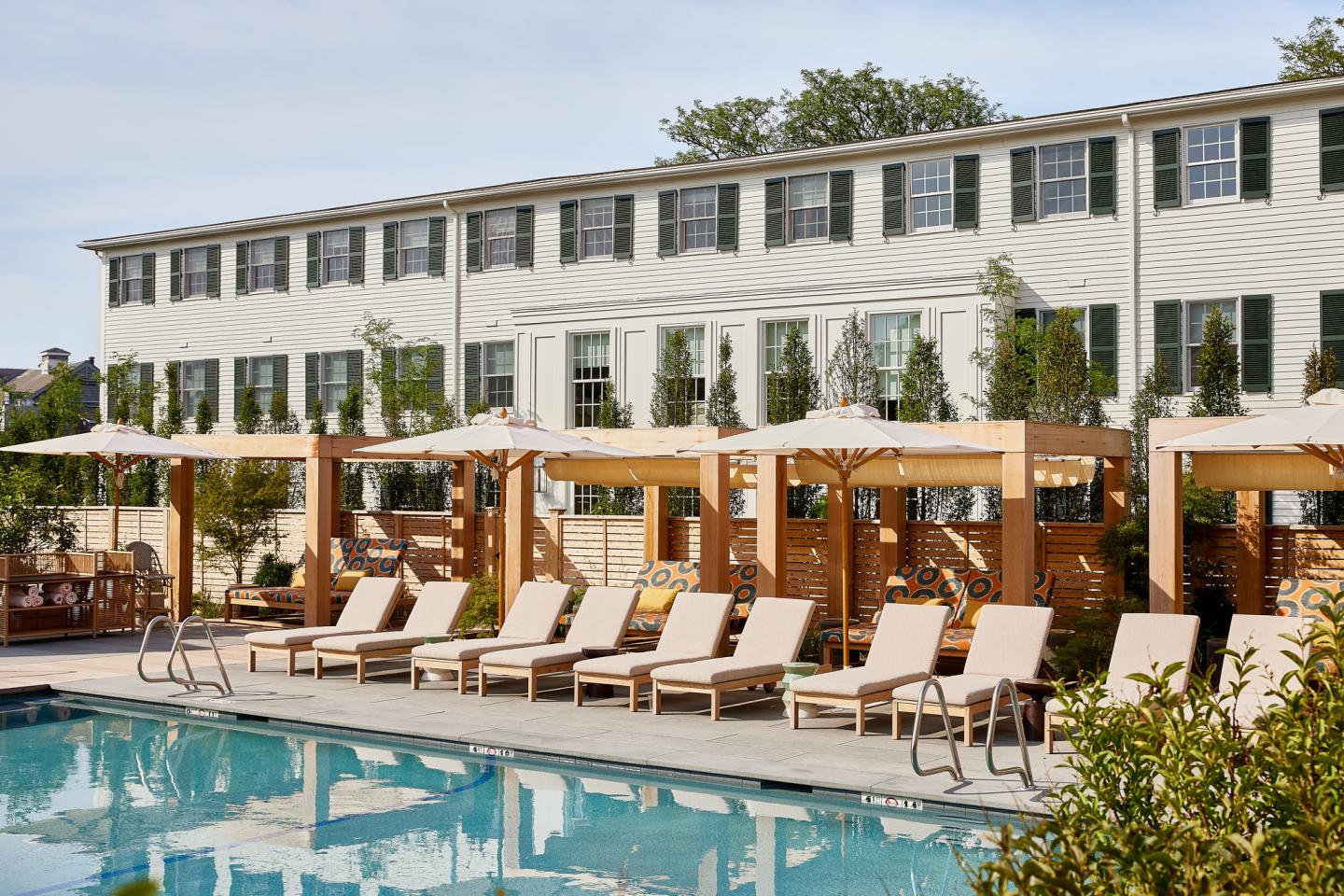 Poolside lounge chairs and umbrellas at a resort with a white building backdrop.