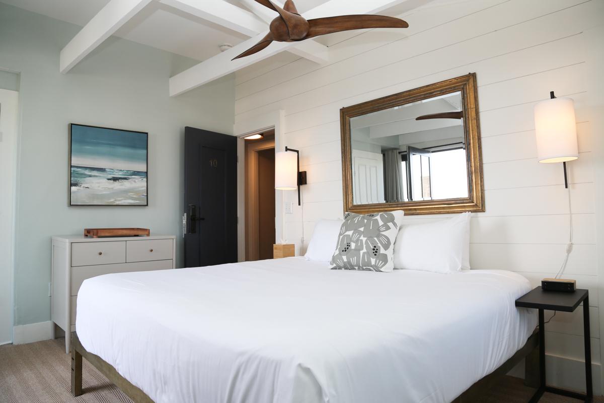 Cozy bedroom with a white bed, beach artwork, and wooden fan.