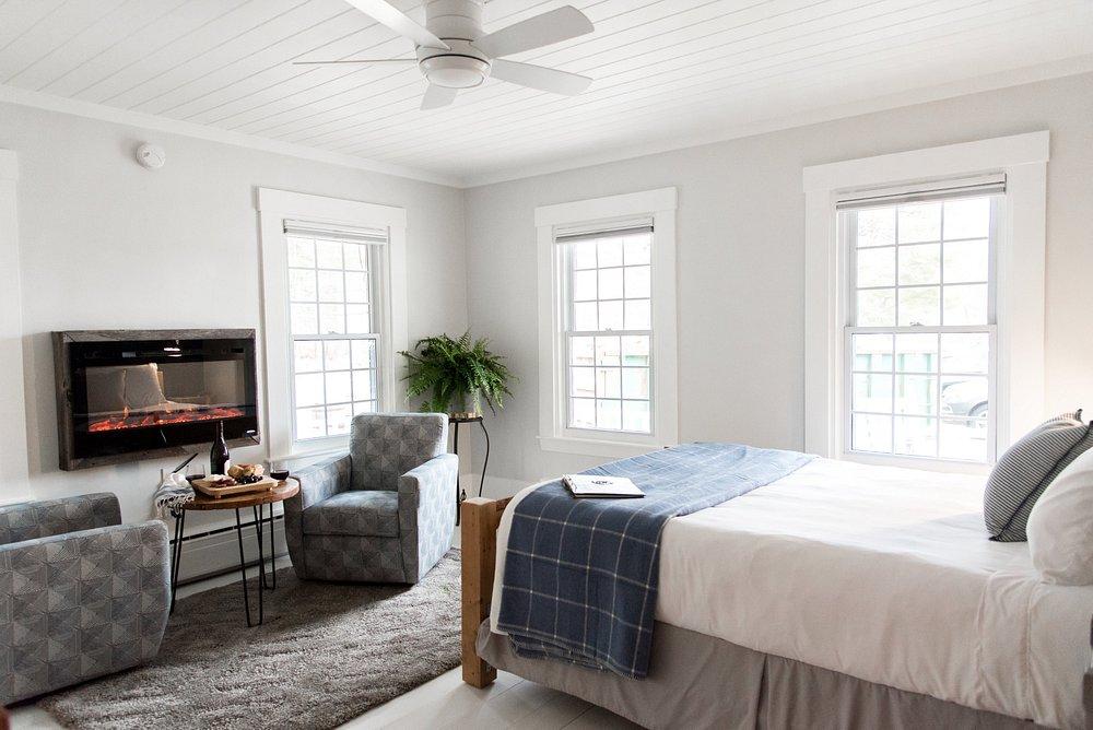 Bright bedroom with a bed, two chairs, and a wall fireplace.