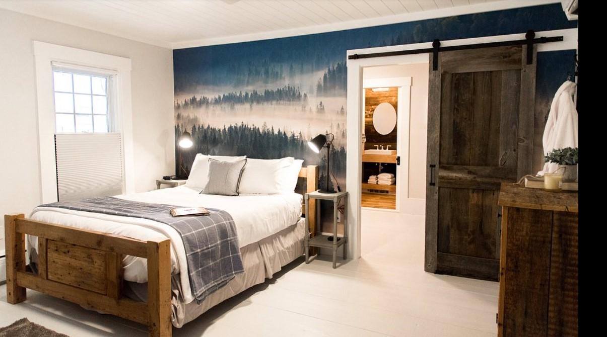 Cozy bedroom with wooden bed, forest mural, and sliding barn door.