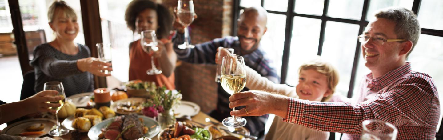 Family cheers with wine glasses around a dining table.