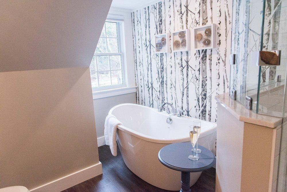 Freestanding bathtub with birch wallpaper and side table with glass.