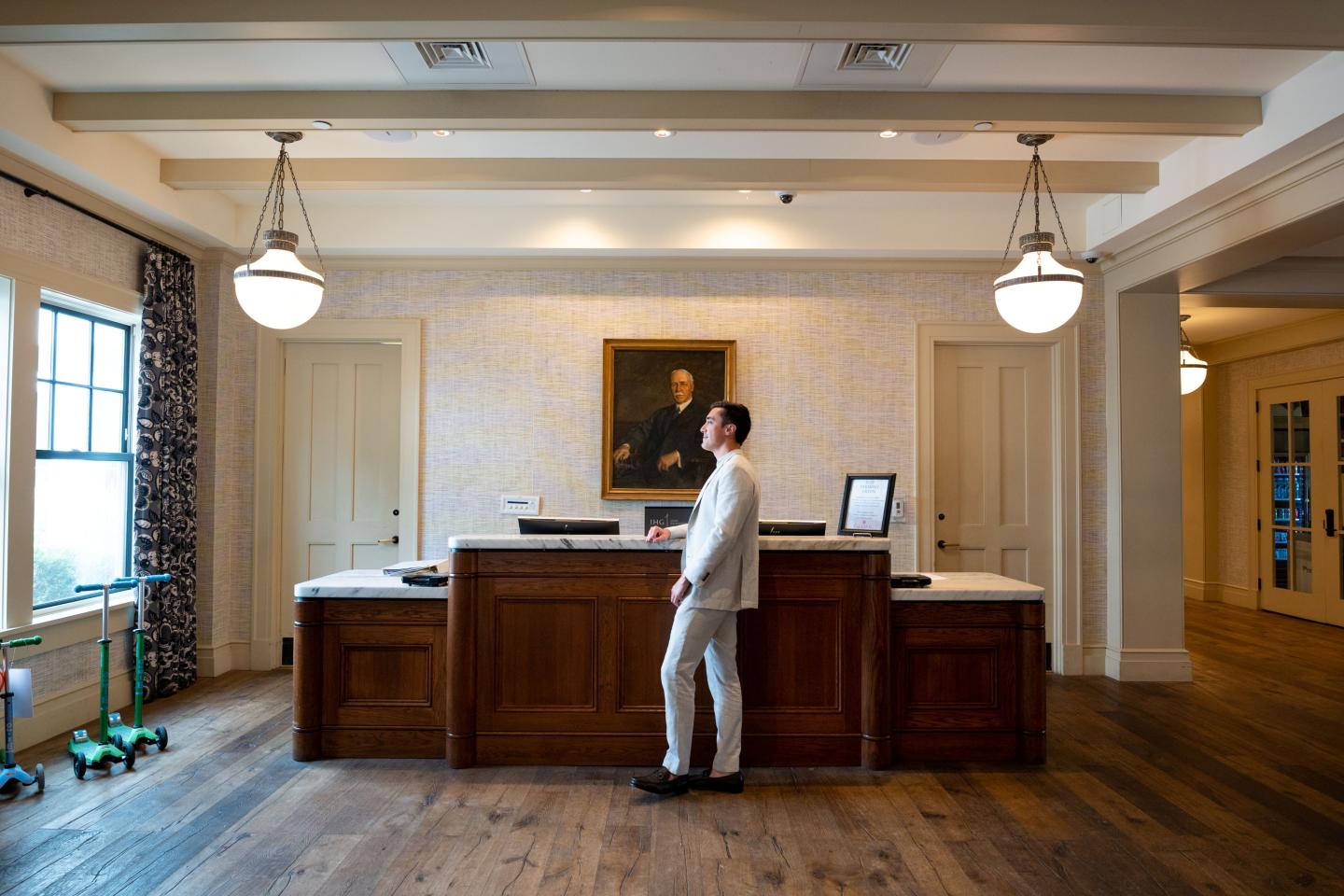 Reception area with a man in a white suit standing by a wooden desk, lit by hanging lamps.